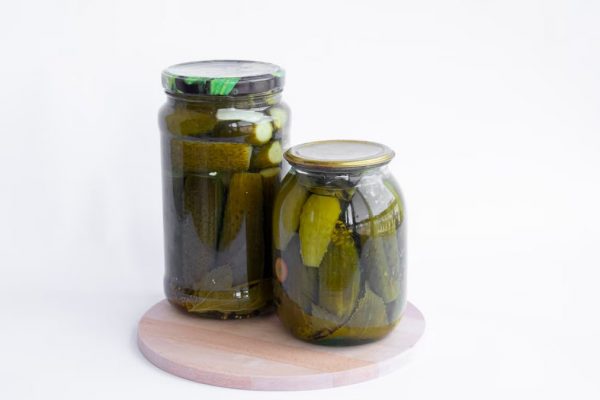 Two jars of pickles sit on a wooden board, showcasing preserved cucumbers in a still life composition.