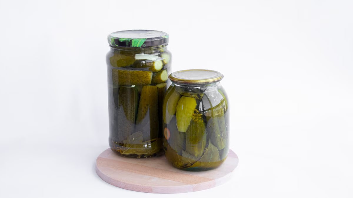 Two jars of pickles sit on a wooden board, showcasing preserved cucumbers in a still life composition.